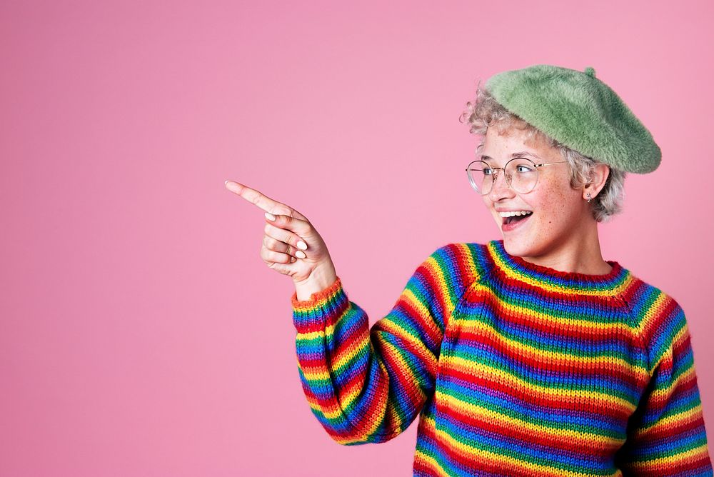 Portrait of a cute cheerful girl wearing glasses pointing side ways in a pink background