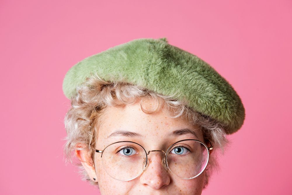 Studio portrait of a young girl wearing glasses and a greet beret in a pink background