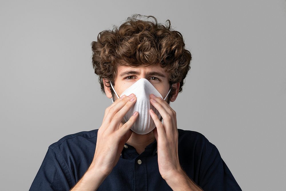 Young man wearing a pollution mask standing by a gray wall mockup 