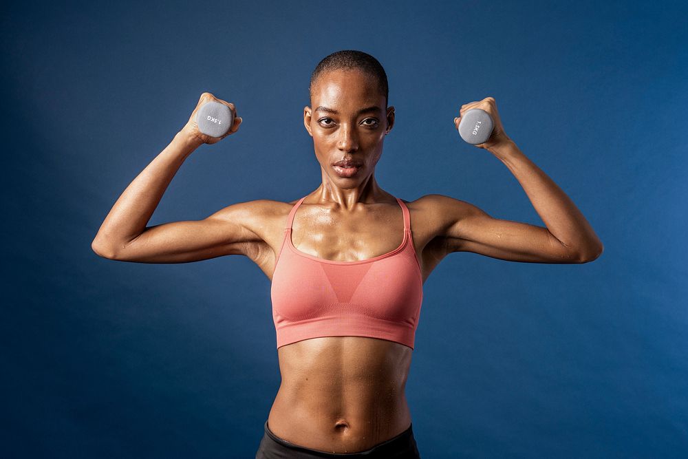 Active black woman lifting dumbbells on blue background