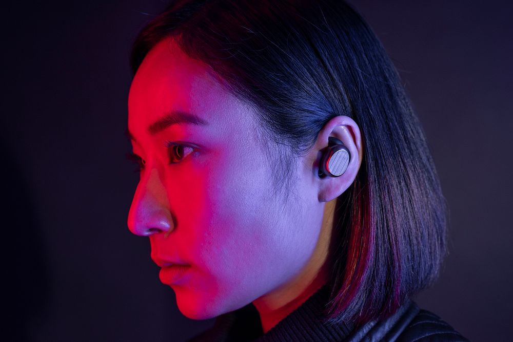 Woman listening to music with wireless earbuds in neon light