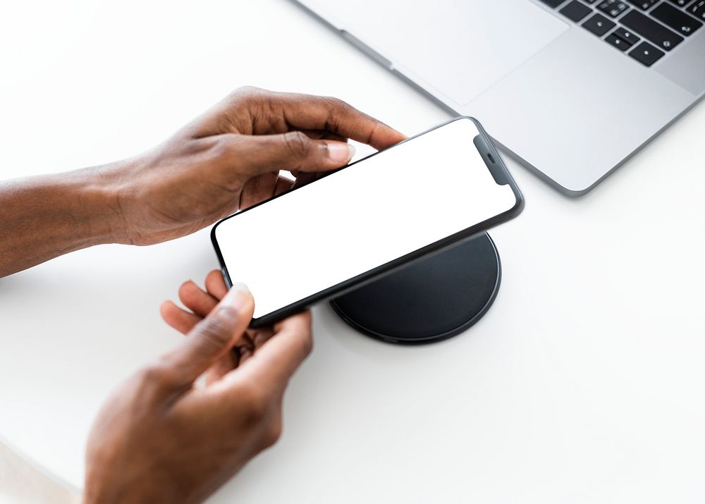 Smartphone screen mockup psd with wireless charger next to laptop