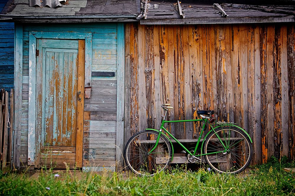 Green bicycle standing on an extreme rough wooden wall, which had once a blue door.Esperanto: Verda biciklo staranta kontaŭ…