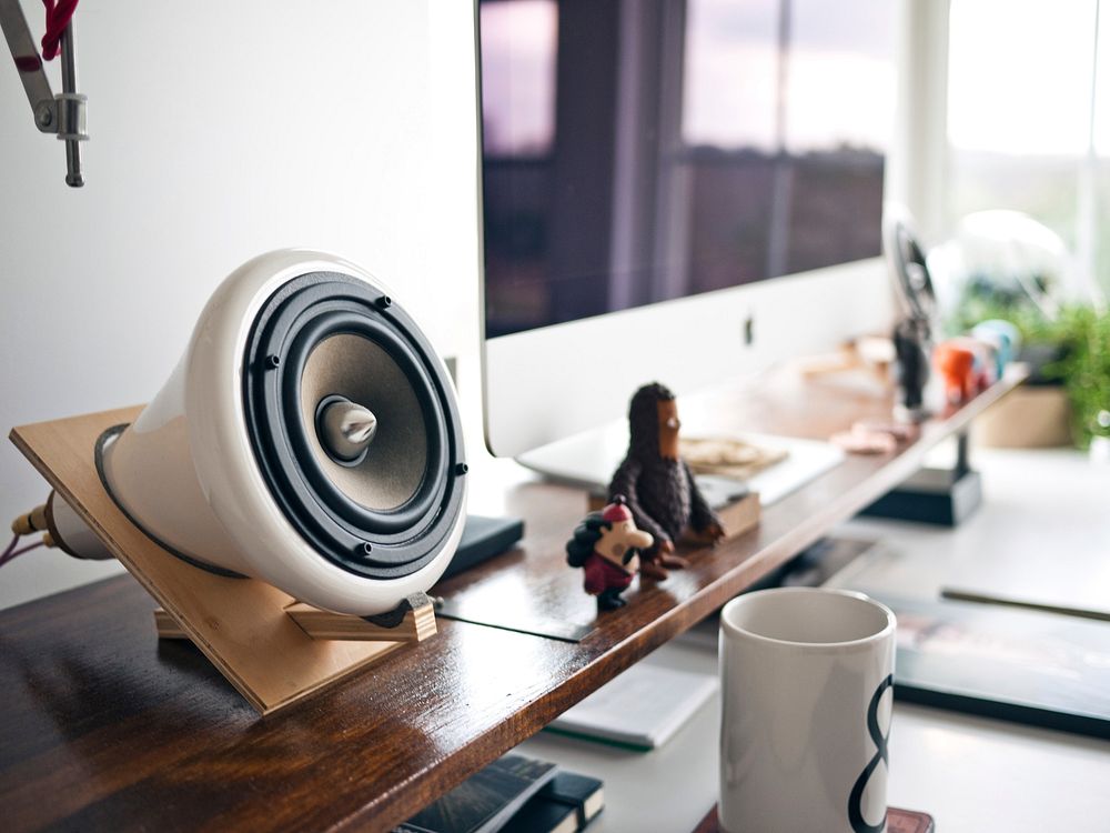 A busy office desk with a sophisticated display of technological devices including computer, music players, speaker and a…