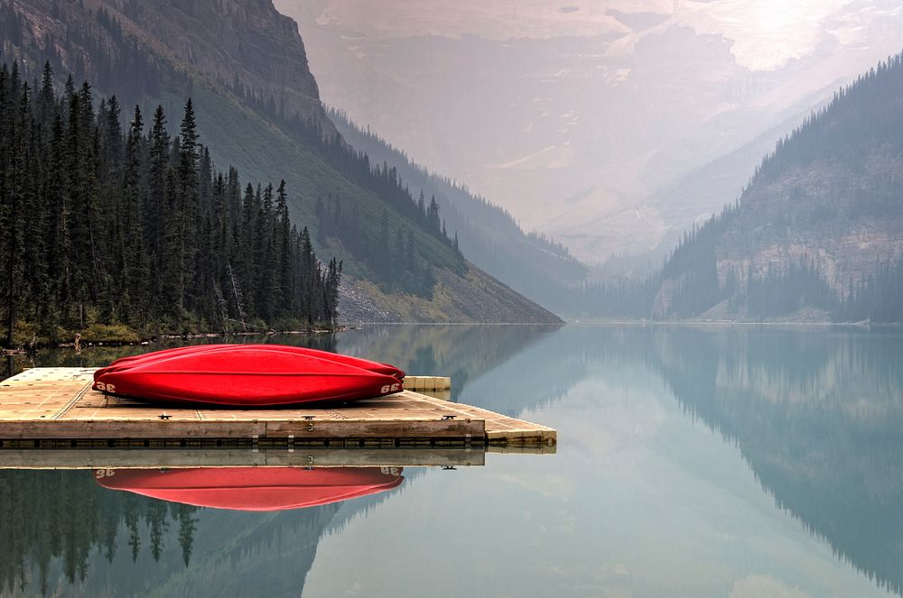 A bright red canoe sits on a wooden dock on a serene Lake Louise. Original public domain image from Wikimedia Commons