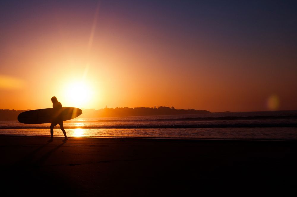 A silhouette of a man walking along the shore as the sun sets over the horizon at Seven Mile Beach. Original public domain…