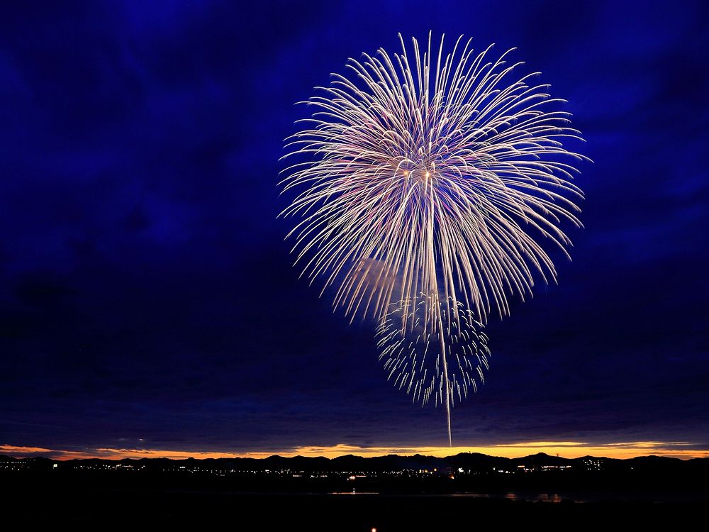 Beautiful fireworks against dark clouds above a city. Original public domain image from Wikimedia Commons