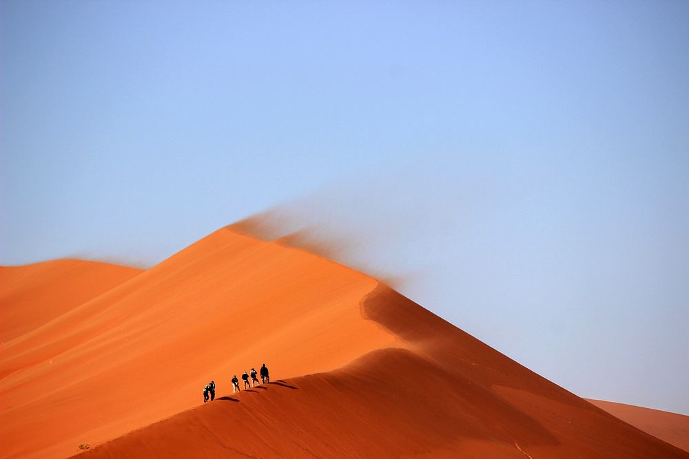 Hikers walk along orange sand ridges on a windy foggy day. Original public domain image from Wikimedia Commons