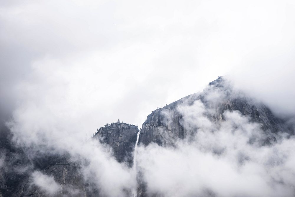 Clouds cover rocky mountain cliffs in the wild. Original public domain image from Wikimedia Commons