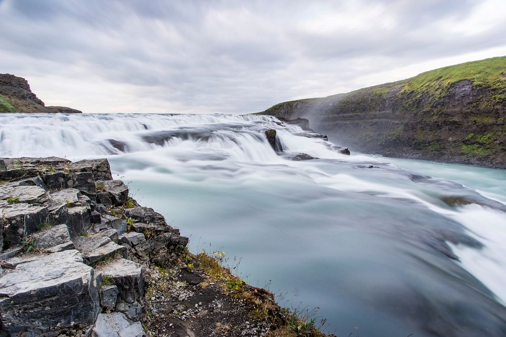 A low waterfall with foamy water flowing down between mossy rocks. Original public domain image from Wikimedia Commons