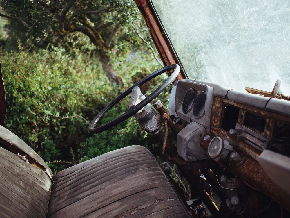 Interior shot of rusty old vehicle with worn seats parked near trees. Original public domain image from Wikimedia Commons