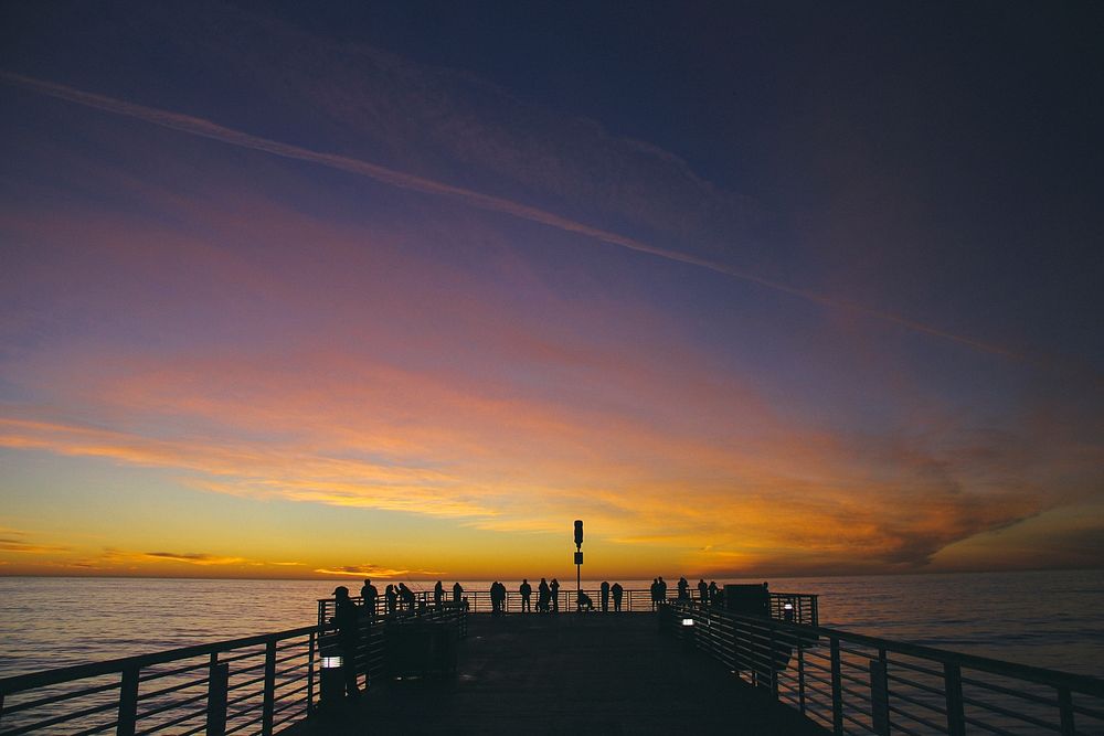 Silhouette of people against a gold sunset at the end of a pier.. Original public domain image from Wikimedia Commons