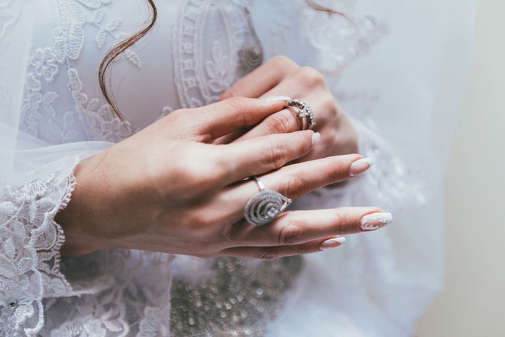 Texas bride touches her wedding ring on finger in front of white lace wedding dress. Original public domain image from…