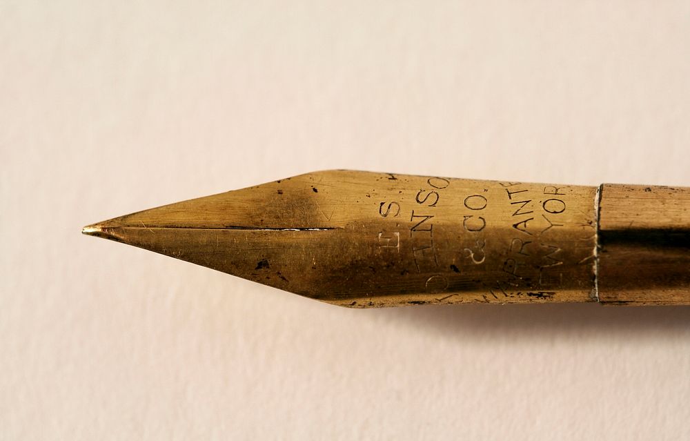 A macro shot of the nib of a fountain pen with letters etched into it. Original public domain image from Wikimedia Commons