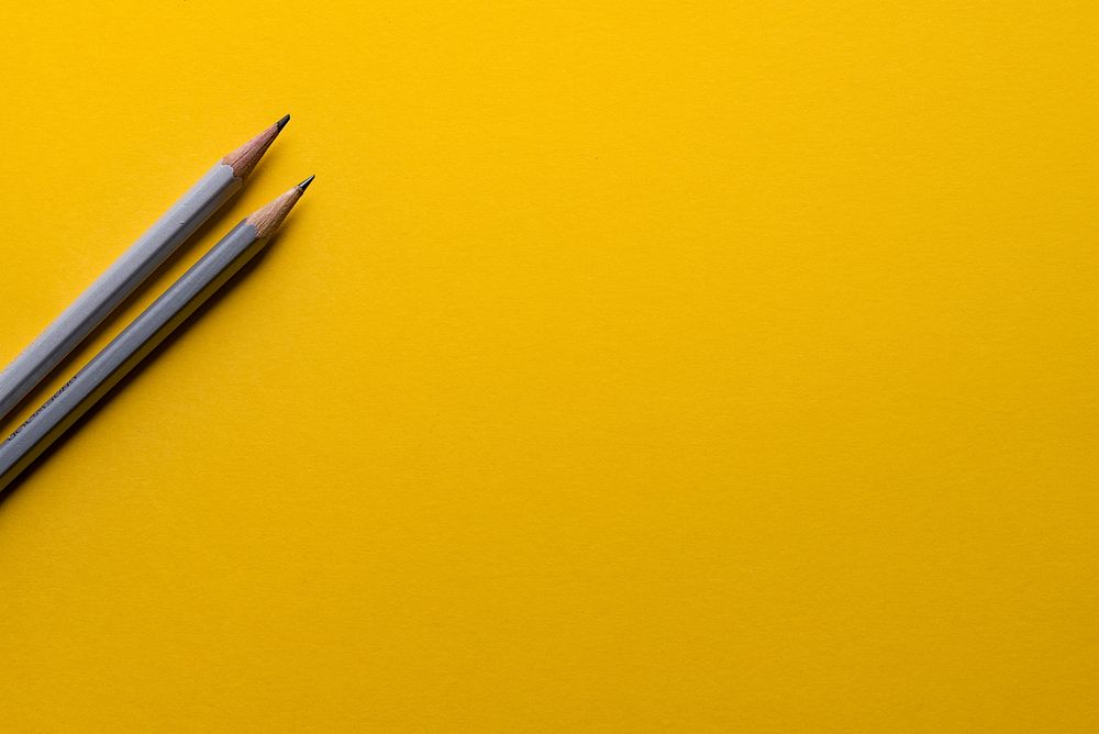 Two gray pencils on a yellow surface. Original public domain image from Wikimedia Commons