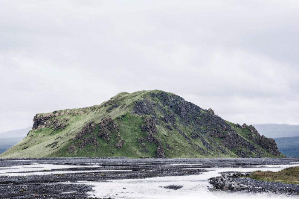 A rugged green hillock in the middle of an icy field in Iceland. Original public domain image from Wikimedia Commons