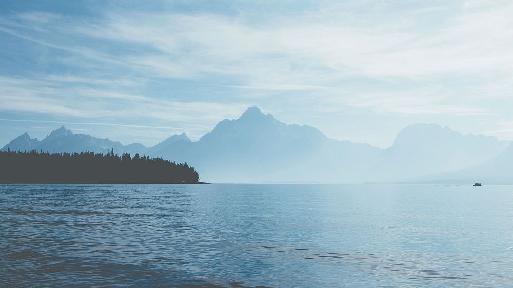 View from a lake on the silhouettes of tall mountains behind fog in Grand Teton National Park. Original public domain image…
