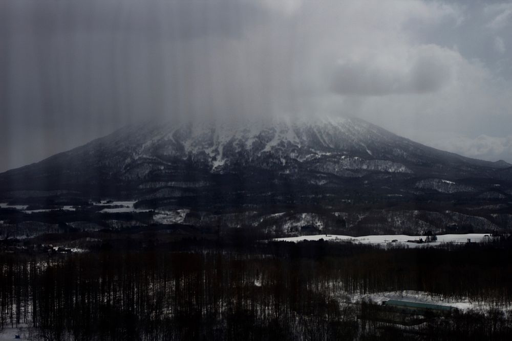 A massive mountain towering over wintry landscape as clouds gather around its peak. Original public domain image from…
