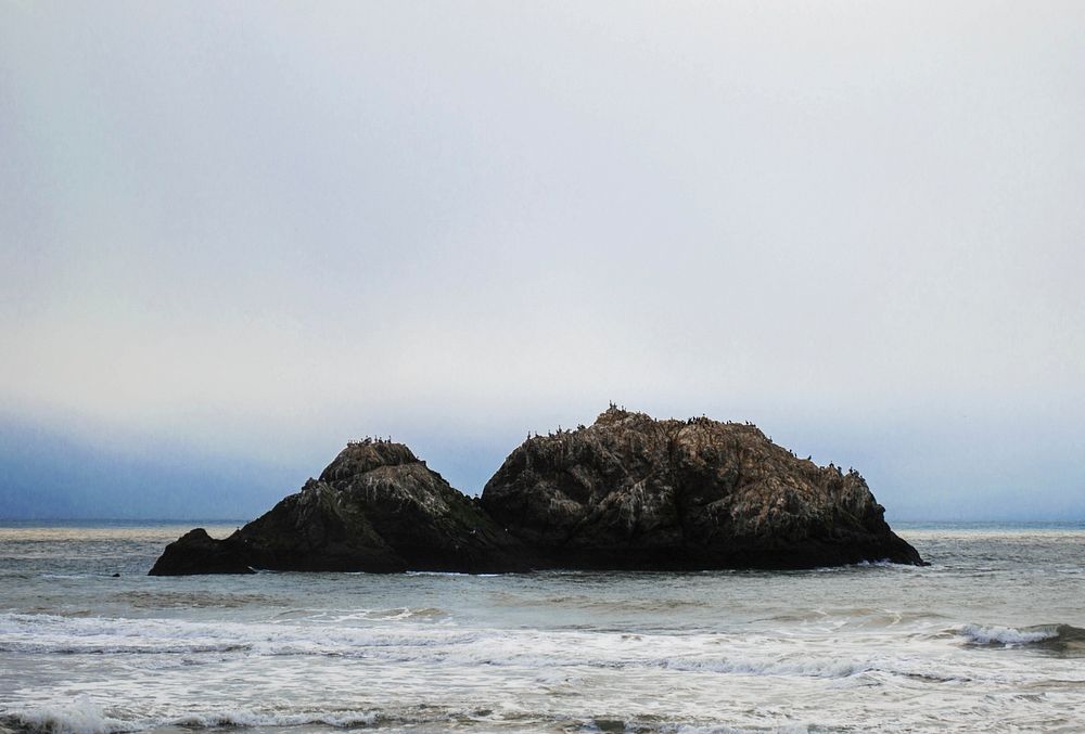 A rocky outcrop in the middle of a rough see. Original public domain image from Wikimedia Commons