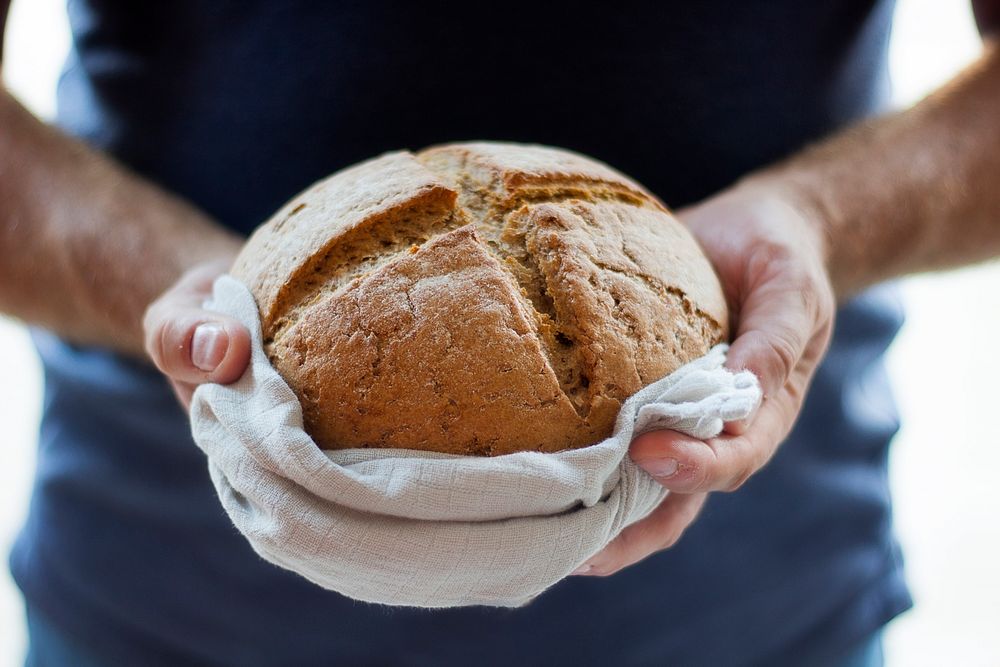 Hands holding a freshly baked loaf of bread in a towel. Original public domain image from Wikimedia Commons