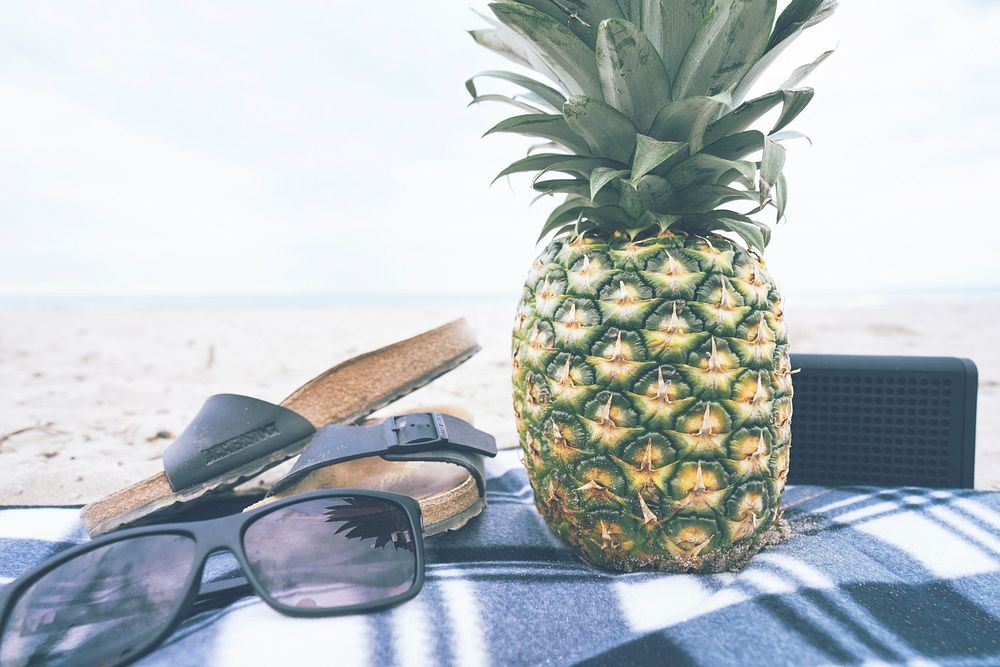 Fresh pineapple, sunglasses, flip-flops, and a Bluetooth speaker on the beach. Original public domain image from Wikimedia…