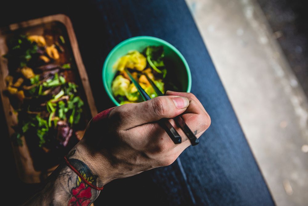 Hand with a tattoo eating salad and pasta with chopsticks. Original public domain image from Wikimedia Commons