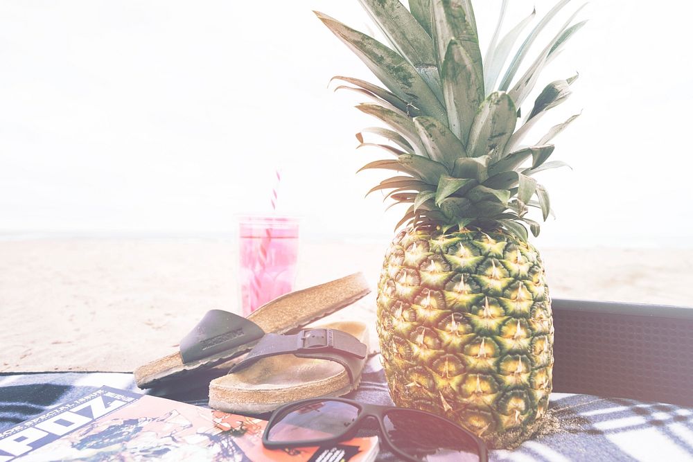 Capture of a juicy looking pineapple beside a sandal with pink sunglass and magazine Port Stanley. Original public domain…