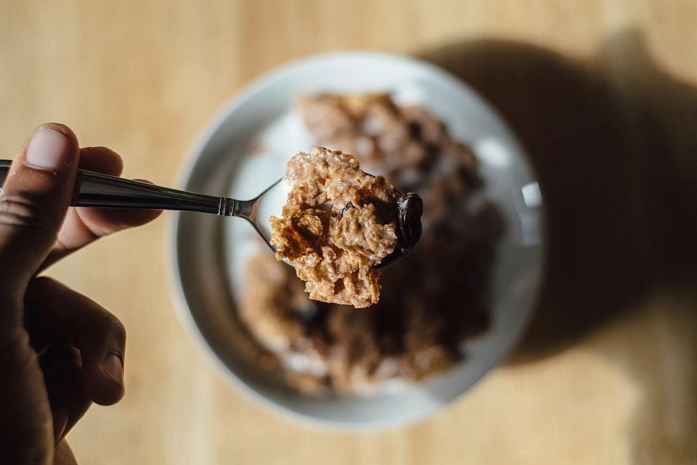 A person holding a spoon full of cereal over a bowl of cereal and milk. Original public domain image from Wikimedia Commons