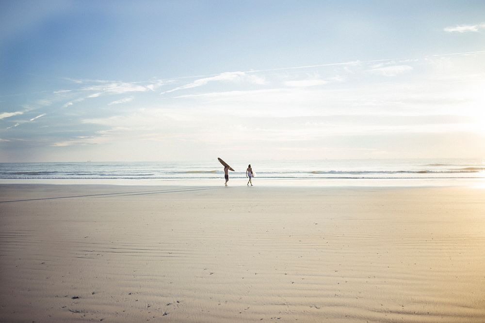 Two surfers walking on the sandy beach towards the ocean. Original public domain image from Wikimedia Commons