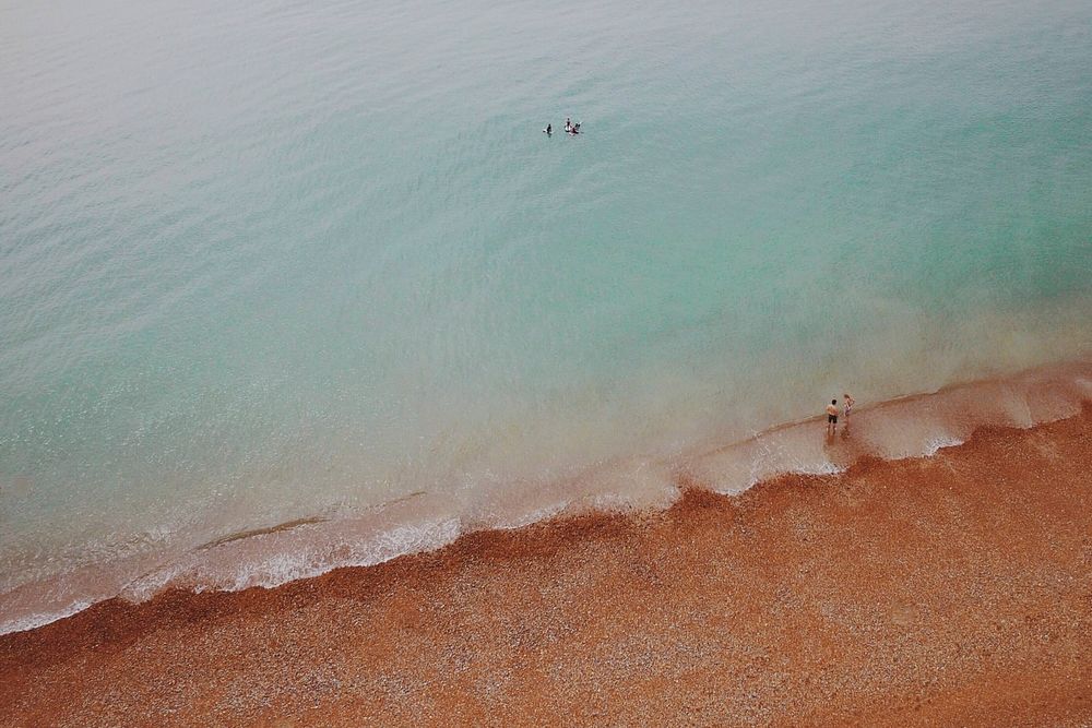 Drone view of people swimming in clear ocean washing up on red sand beach in Brighton. Original public domain image from…