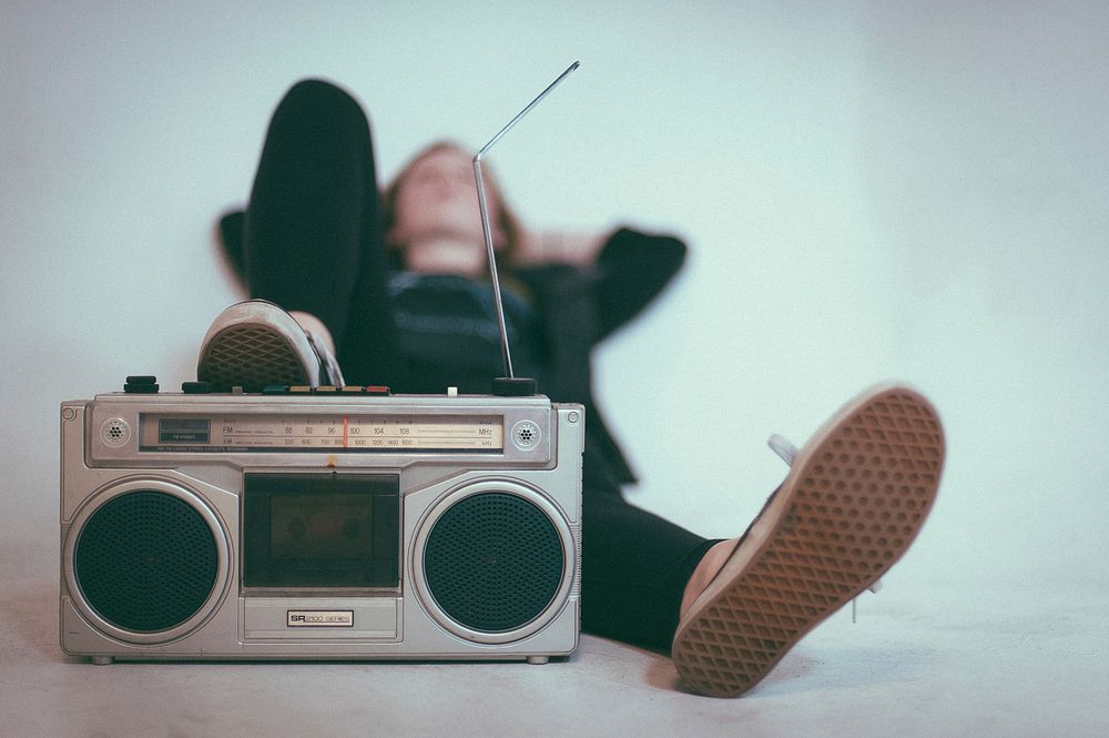 A blurry shot of a woman in sneakers reclining with her foot on a vintage sound system. Original public domain image from…