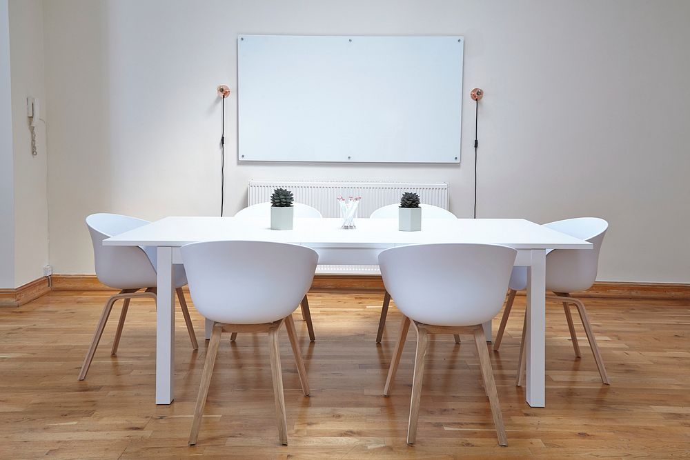 White chairs near a white table in a small conference room with a whiteboard. Original public domain image from Wikimedia…