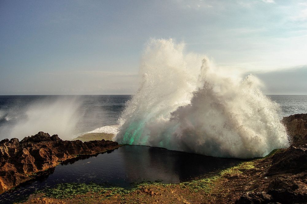 An ocean wave hitting rocks and creating spray on the coast. Original public domain image from Wikimedia Commons