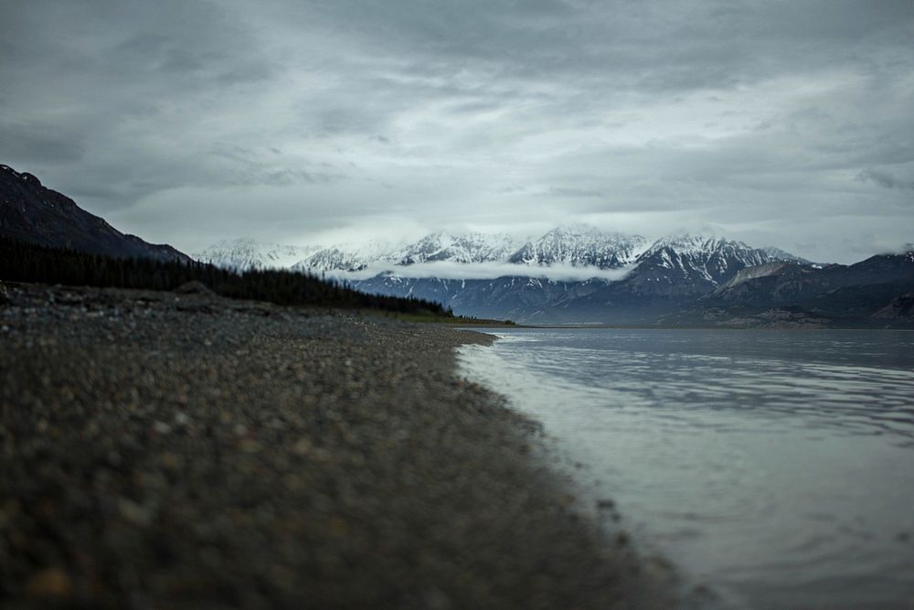 A rocky beach by a lake at Yukon with snowy mountains in the distance. Original public domain image from Wikimedia Commons