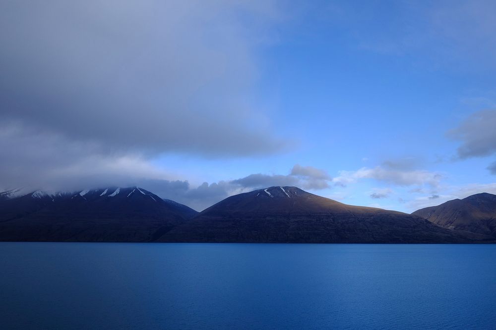 The calm surface of Lake Ohau by a mountain range under clouds. Original public domain image from Wikimedia Commons