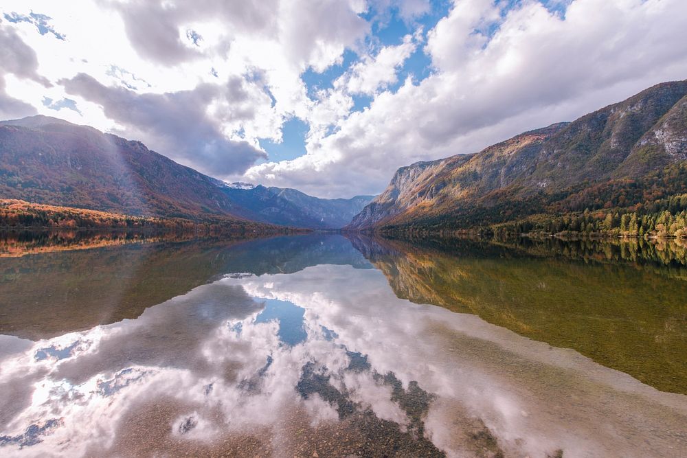 The clear surface of Lake Bohinj in the mountains reflecting the white clouds above. Original public domain image from…