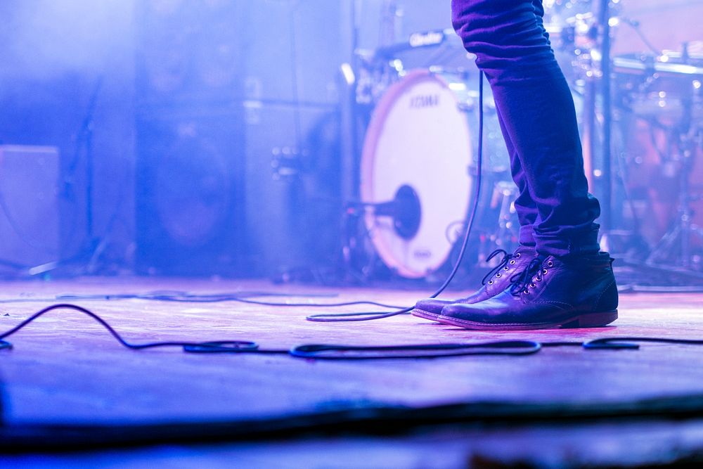 A low shot of a musician's jeans and shoes on a stage. Original public domain image from Wikimedia Commons
