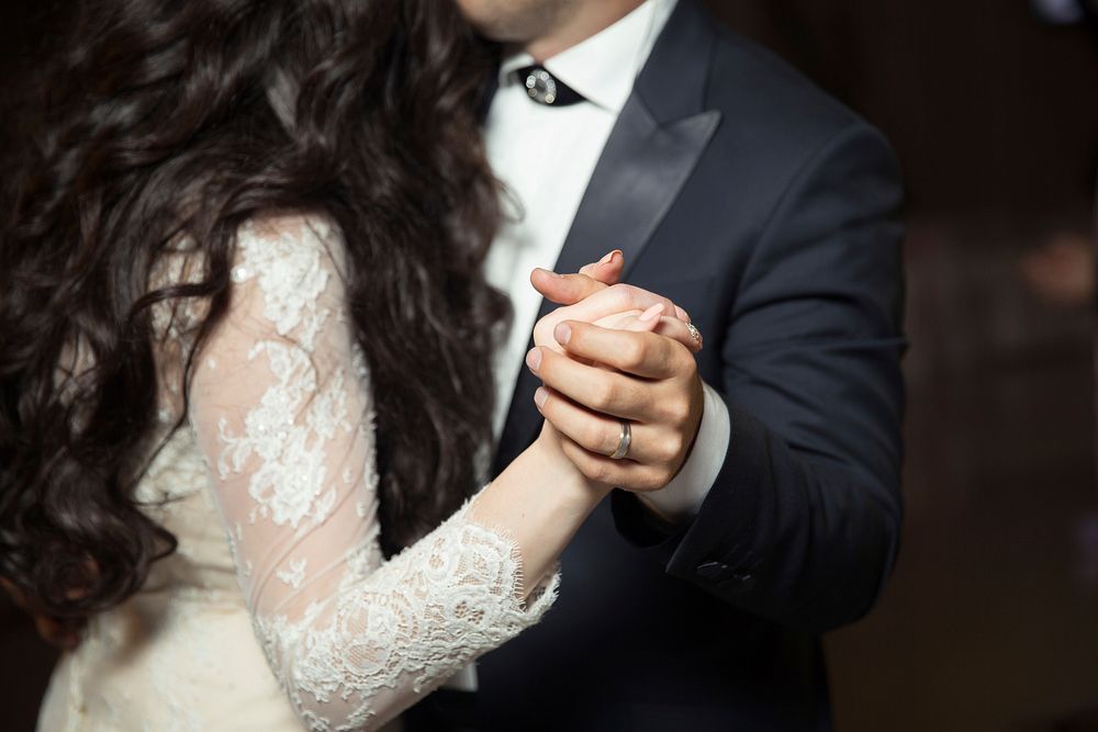 A bride and a groom slow dance, holding hands, at their wedding. Original public domain image from Wikimedia Commons
