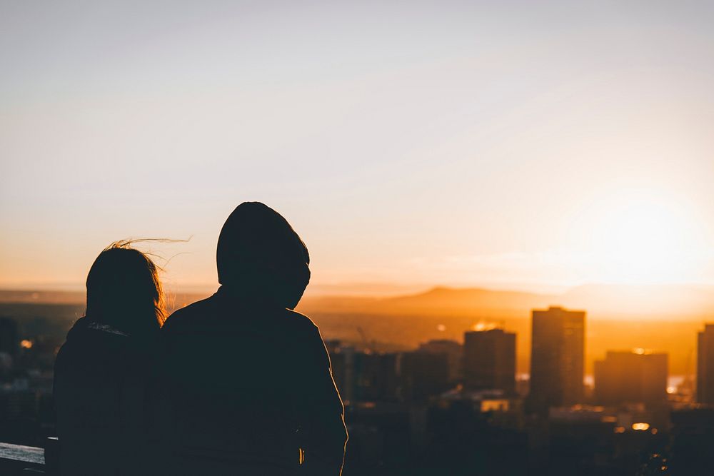 Silhouettes of two people looking over a cityscape during sunset. Original public domain image from Wikimedia Commons