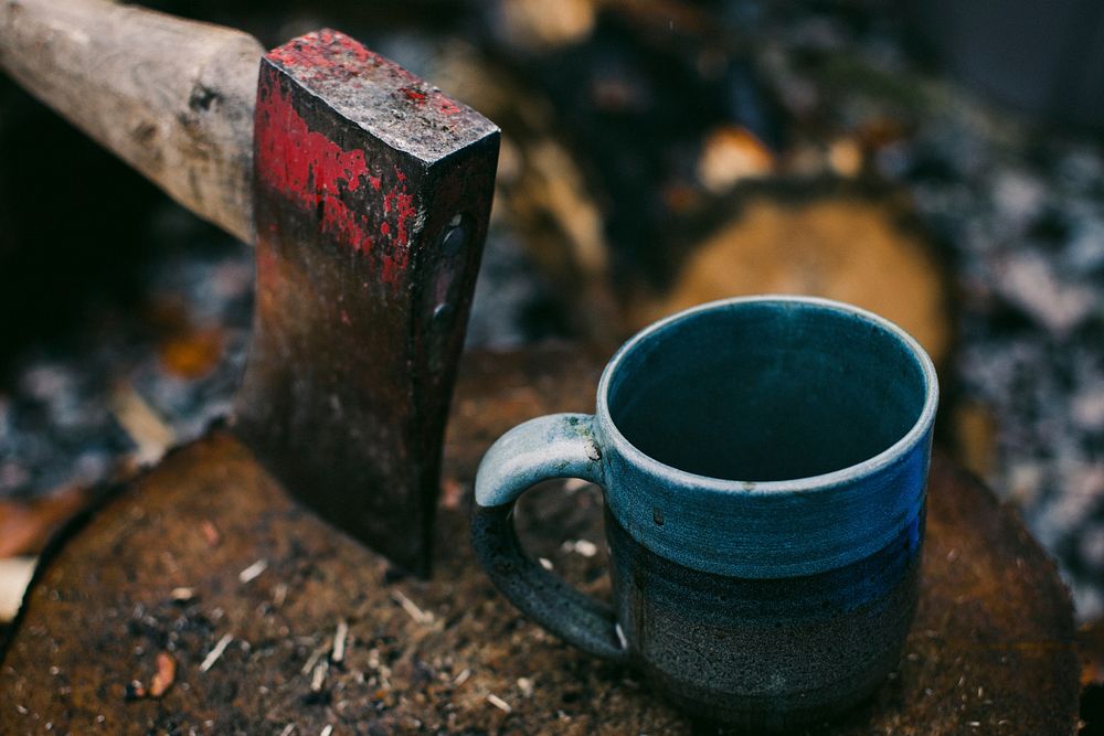 A blue enamel cup next to a rusty axe on a log. Original public domain image from Wikimedia Commons