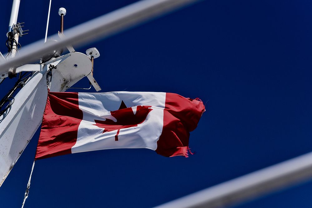 Canadian flag flying on a flagpole by industrial beams. Original public domain image from Wikimedia Commons
