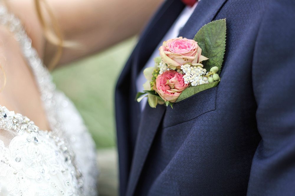 A small bouquet of roses and tiny white flowers in the buttonhole of a groom's suit. Original public domain image from…
