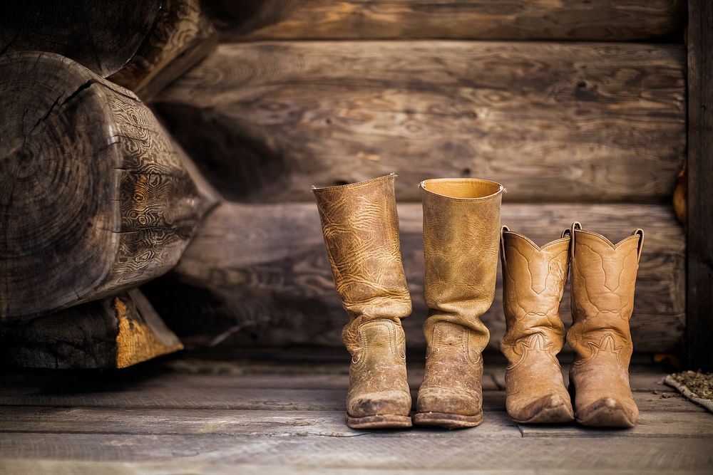 Two pairs of worn in cowboy boots set in front of wooden logs. Original public domain image from Wikimedia Commons