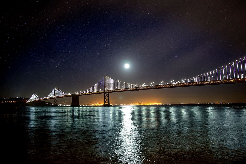 Moon over the San Francisco – Oakland Bay suspension Bridge reflected on the water below. Original public domain image from…