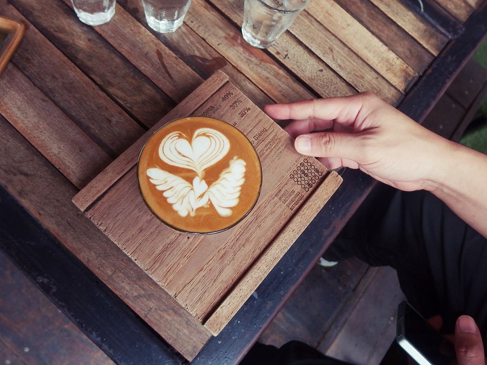 Angel wings and a heart formed the art of a cup of latte served on wood.. Original public domain image from Wikimedia Commons
