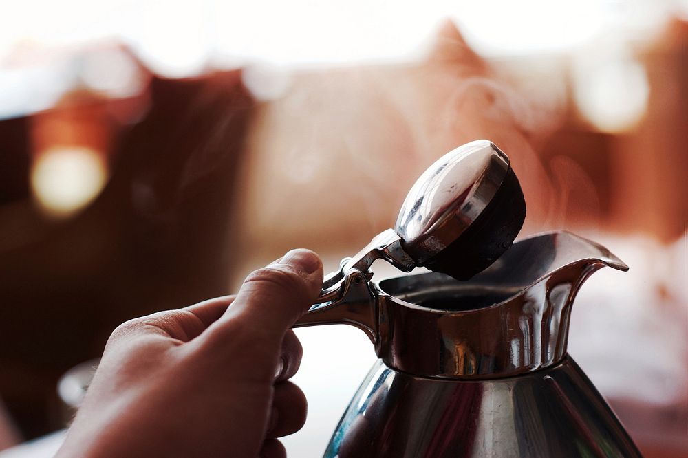 A coffee pot being held and opened to allow steam to escape. Original public domain image from Wikimedia Commons