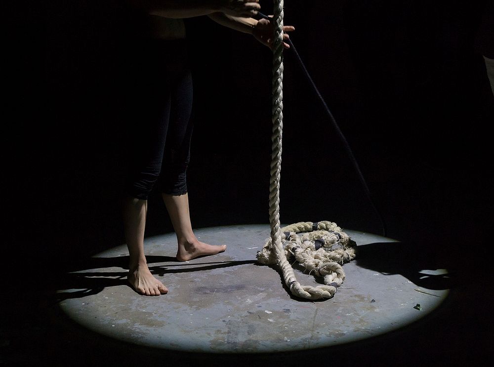 A barefoot person holding rope under a spotlight. Original public domain image from Wikimedia Commons