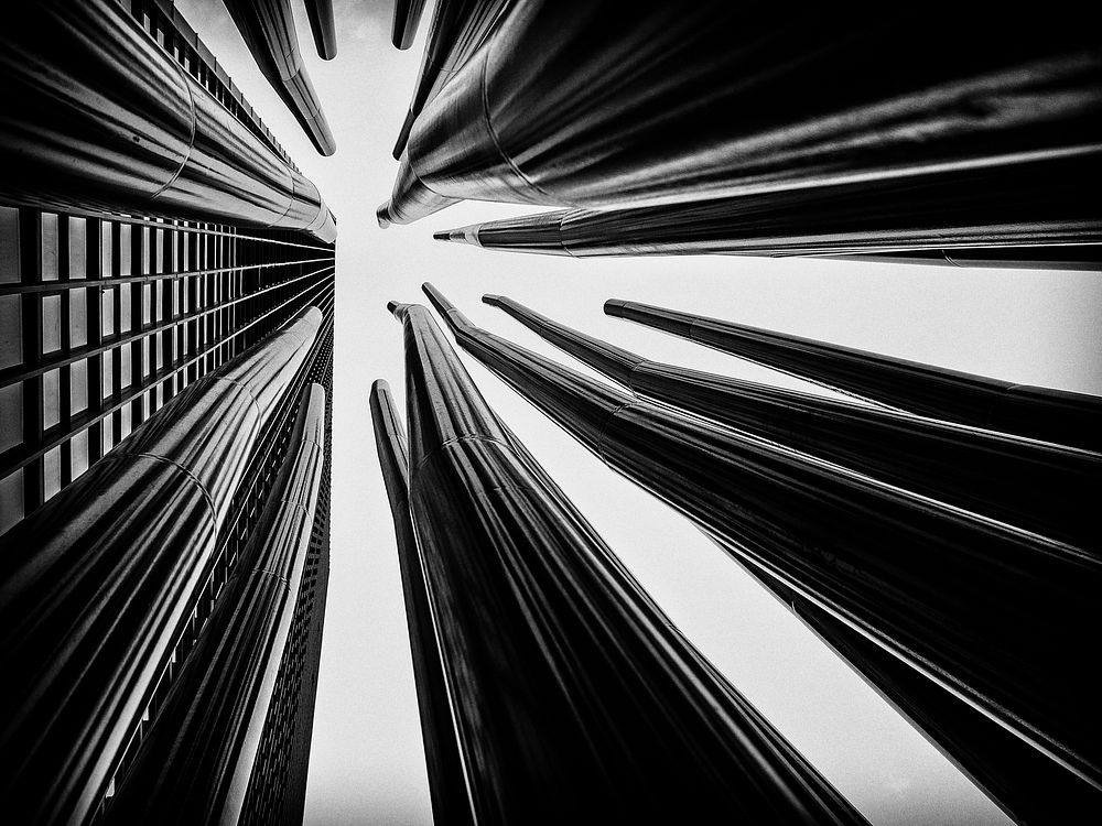 A number of twisted metal tubes rising up towards the sky next to a tall building. Original public domain image from…