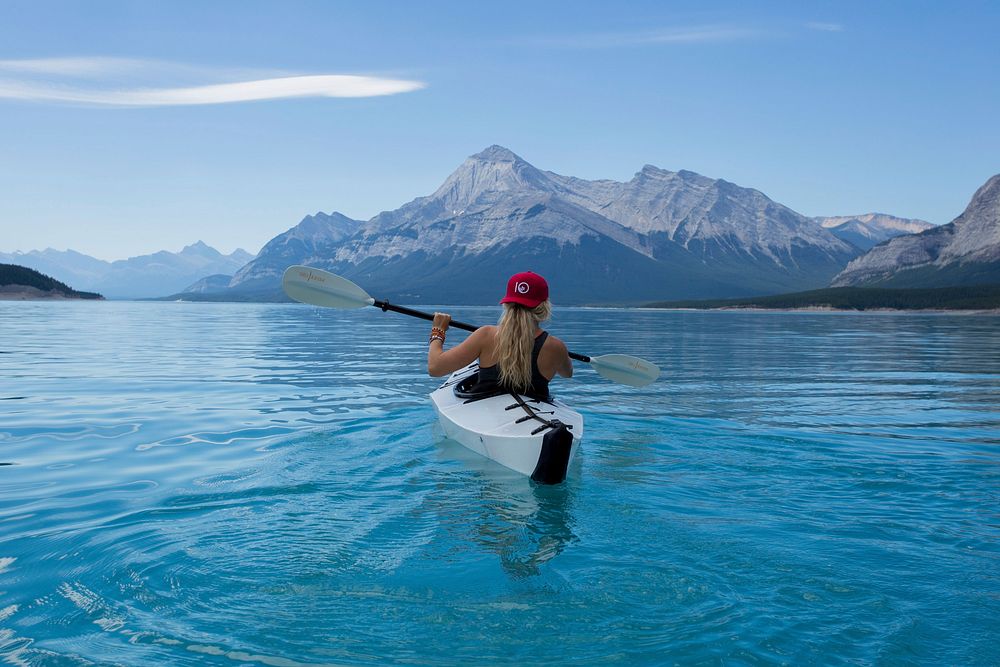 Woman wearing red hat riding on white kayak facing mountain alps. Original public domain image from Wikimedia Commons