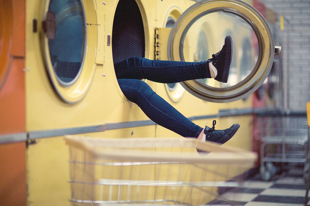 A person's legs sticking out of a large washing machine. Original public domain image from Wikimedia Commons